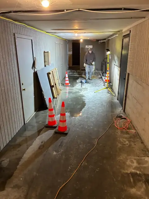 Technician working a slab leak in a commercial basement corridor with cones and work lights