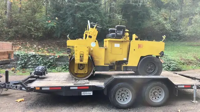 Vibratory roller compactor loaded on an Eagle equipment trailer in a wooded Kitsap driveway
