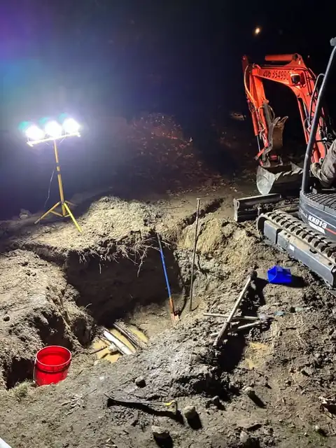 Tripod work lights and a mini excavator over a large night excavation