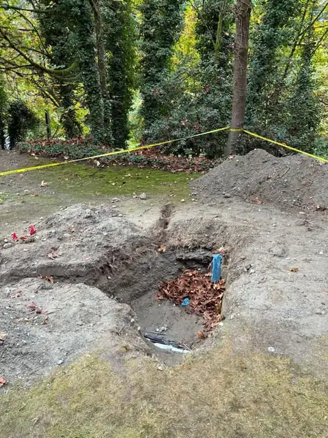 Deep excavation pit exposing old pipes behind caution tape