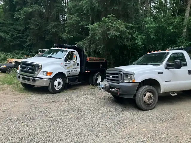 Ford F-650 dump truck and F-350 flatbed parked on gravel at the equipment yard