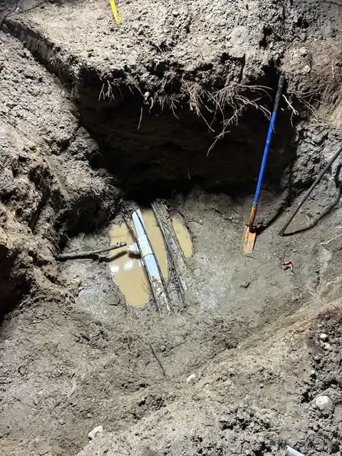 Exposed pipes sitting in water at the bottom of a pit lit by work lights