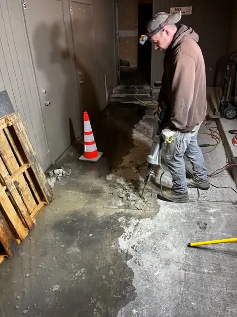 Technician with a demolition hammer opening a commercial basement slab beside wooden pallets