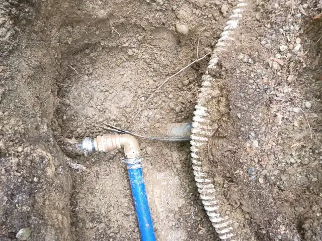 Brass elbow and clamp connecting blue PEX to an older line in a muddy excavation