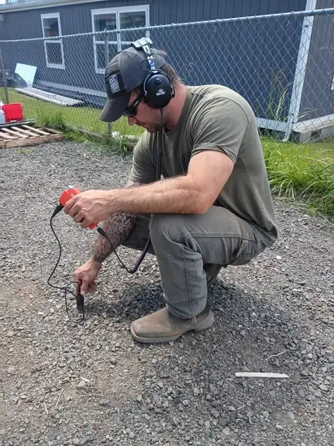 Leak detection technician with headphones pressing an acoustic sensor to gravel to locate a buried leak