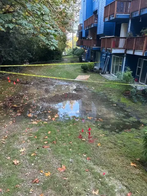 Condominium lawn with standing water and an excavation marked with cones and flags