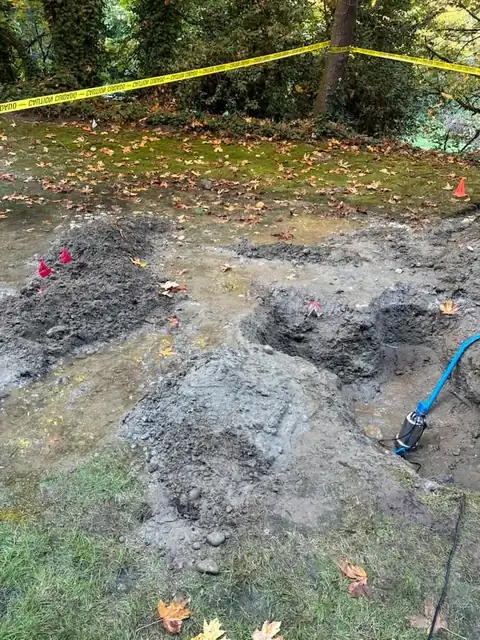 Mounds of excavated soil beside a flooded pit with a pump