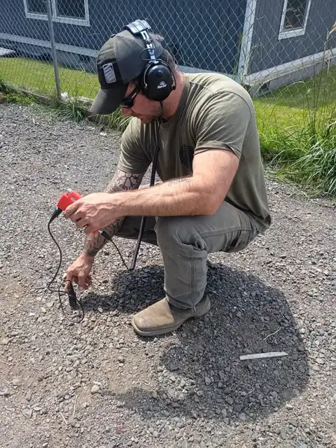 360 Leak Finders technician crouched on gravel using an acoustic ground microphone and headphones to pinpoint an underground water leak