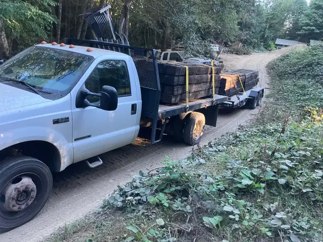 F-350 flatbed truck and trailer hauling timbers down a forest road