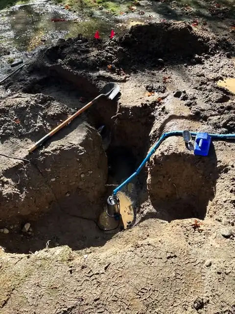 Excavation pit with pump and shovel beside a muddy lawn