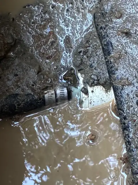 Leaking pipe clamp and fitting submerged in muddy water at the bottom of an excavation