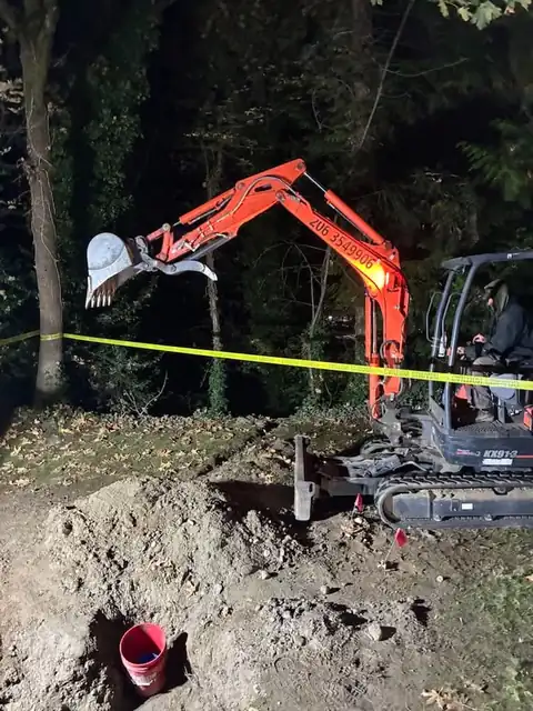 Mini excavator boom raised over a night excavation with caution tape