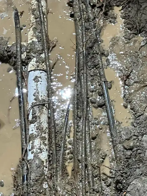 Old white PVC pipe and conduit exposed in muddy water in an excavation