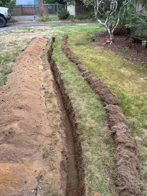 Clean machine-cut trench across a lawn with spoils piled on a tarp beside it
