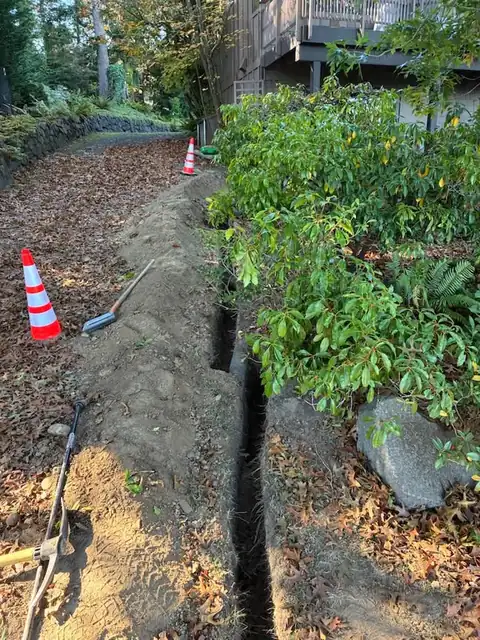 Trench along a stone wall driveway with cones and a shovel