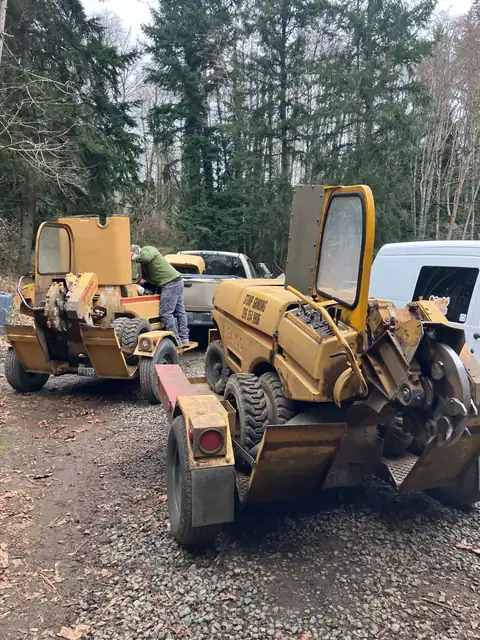 Two Rayco stump grinders with the company phone number at the equipment yard