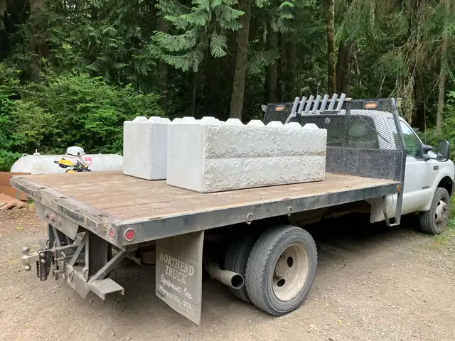 Ford flatbed work truck loaded with concrete ecology blocks on a forested gravel drive
