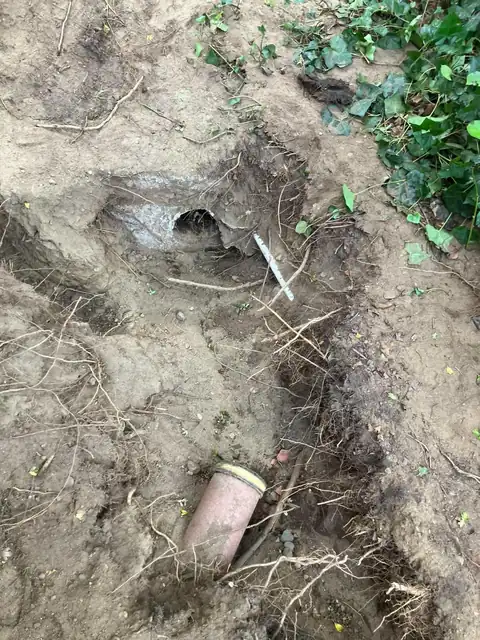 Broken clay drain pipe section and an old pipe end exposed in a dug-out bank