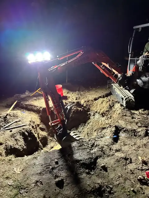 Mini excavator bucket digging under tripod lights at night