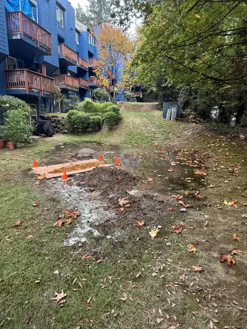 Flooded condominium lawn with cones and plywood around the excavation