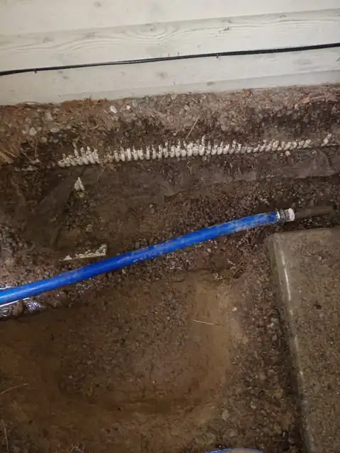 Blue PEX water line laid in a trench along a foundation next to a corrugated drain pipe