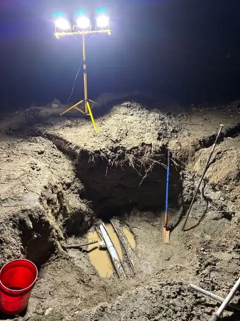 Work light tripod over an excavation pit with exposed pipes at night