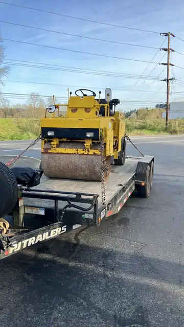 Yellow vibratory roller chained on a PJ Trailers equipment trailer at the roadside