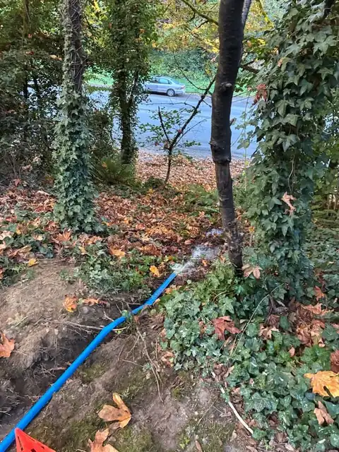 Blue discharge hose carrying pumped water out of an excavation toward the street