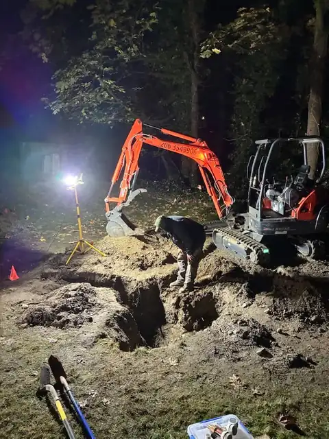 Technician at a night excavation beside the 360 Leak Finders mini excavator