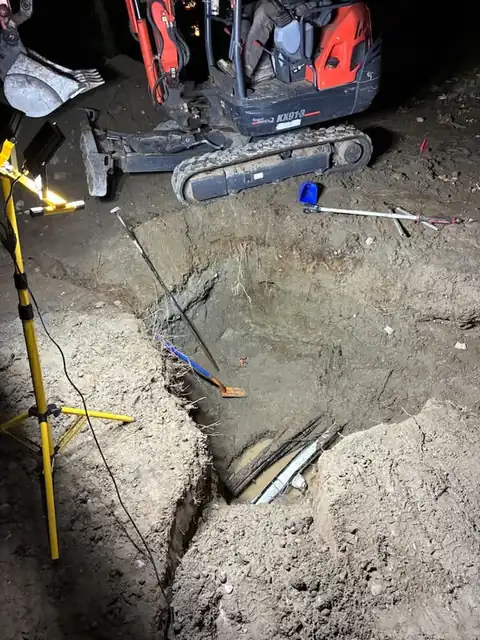 Mini excavator and work light over an excavation pit at night