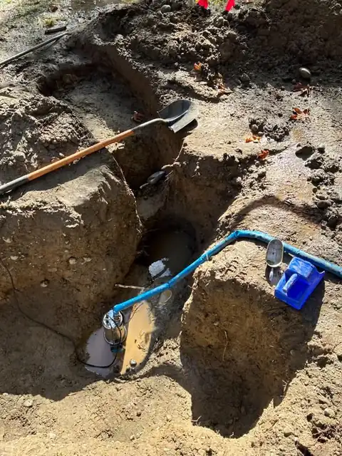 Submersible pump dewatering an excavation pit with blue discharge hose