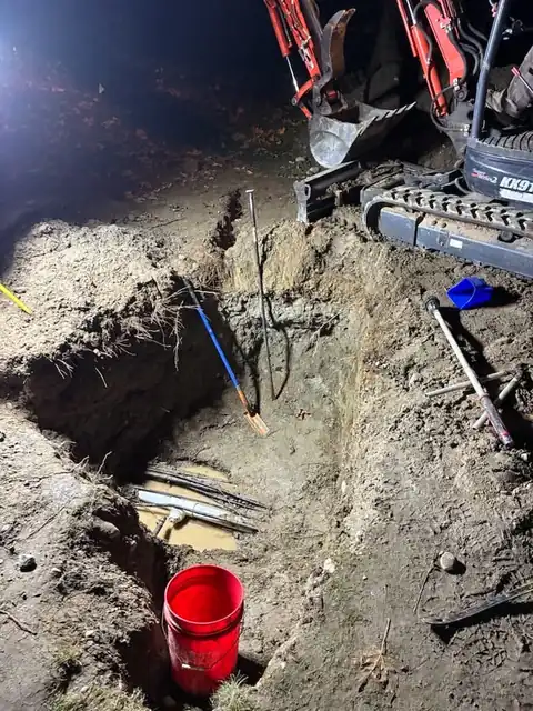 Mini excavator bucket over a lit excavation pit at night