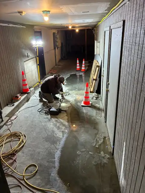 Wide view of a commercial basement hallway during slab leak repair with cones marking the wet zone