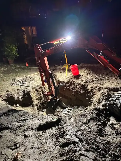 Mini excavator boom silhouetted against work lights at night