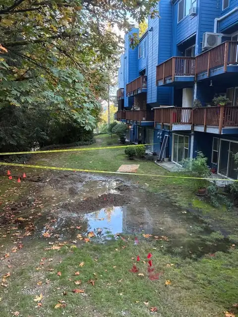 Flooded lawn and taped-off excavation beside a blue condominium building