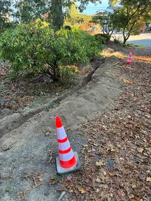 Freshly backfilled trench line through a yard marked with cones
