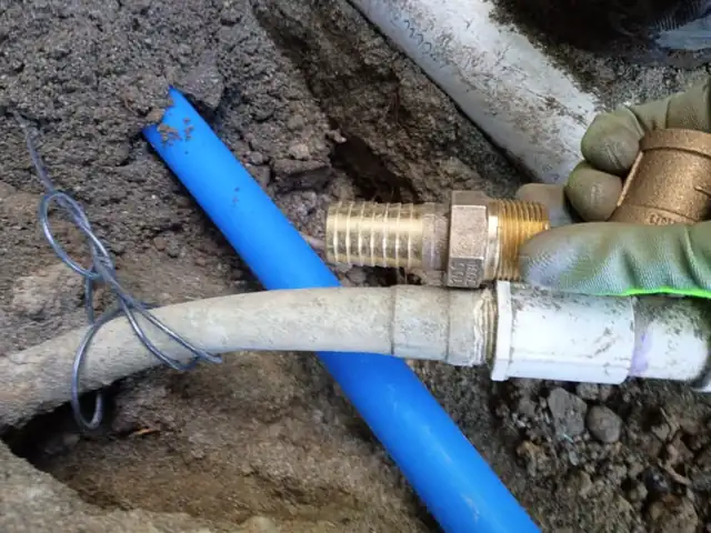 Brass compression fitting joining new blue PEX water line to an existing supply pipe in an open trench