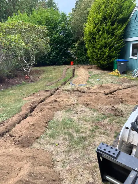 Trench across a backyard lawn with a skid steer in the foreground